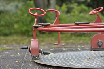 Colorful carousel in park for childrens amusement. Red iron activity equipment on cement platform with wheels and pedals.