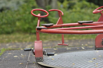 Colorful carousel in park for childrens amusement. Red iron activity equipment on cement platform...