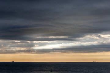 Sunset over the ocean with dramatic clouds, distant ship silhouettes, serene nature landscape at twilight