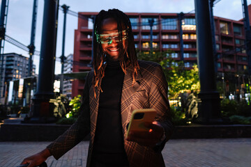 Happy businessman wearing smart glasses and using mobile phone at dusk