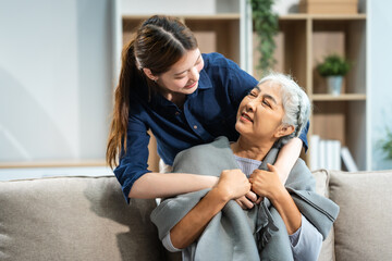 In their living room, a young Asian woman and her grey-haired mature mom, mother and daughter, sit...