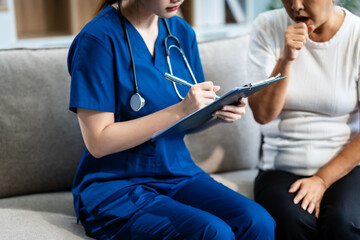 Obraz premium Young Asian nurse attends to older grey-haired mature woman sitting on sofa, conducting health assessment and discussing conditions osteoporosis, arthritis, Alzheimer's disease, dementia, and more.