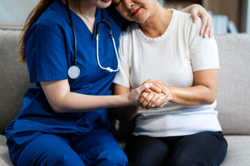 A young Asian nurse, only woman present, holds hands with an older grey-haired mature woman sitting...