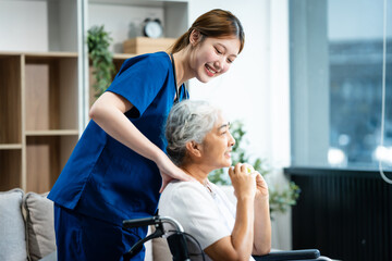 A young Asian nurse, the only woman present, assists an older grey-haired mature woman on a wheelchair sitting on a sofa. They focus on taking a medical history and conducting health checks.