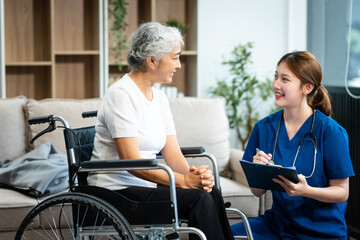 Obraz premium A young Asian nurse, the only woman present, assists an older grey-haired mature woman on a wheelchair sitting on a sofa. They focus on taking a medical history and conducting health checks.