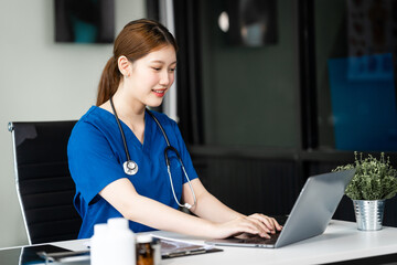 A young female nurse in a blue uniform works alone at a desk in a private room in a children's...