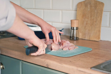 Female butcher cut raw meat with sharp knife at home kitchen. Woman cutting the chicken fillet in pieces for cooking. Preparing chopping food. Split poultry breast. Healthy lean meat, low cholesterol