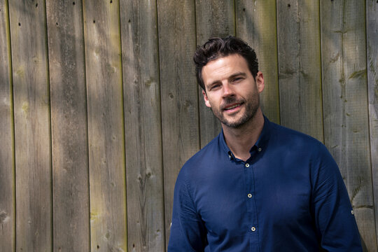 Smiling businessman standing in front of wooden fence