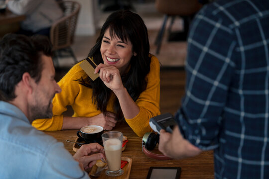 Happy businessman having coffee with colleague paying through credit card in cafe