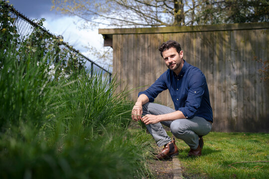 Smiling businessman crouching near plants in front of wall at back yard