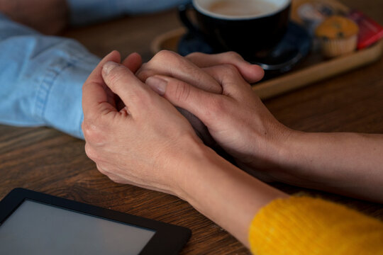Couple holding hands on table near coffee cup and tablet PC in cafe