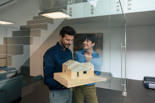 Happy mature businessman standing with model house near businesswoman at home office