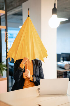 Businesswoman opening yellow umbrella near laptop at desk