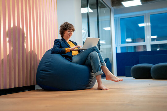 Smiling businesswoman using laptop on bean bag at office