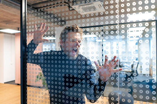 Mature businessman making face over spotted glass in office