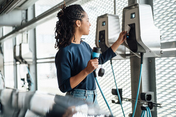 Smiling young businesswoman paying through credit card holding electric plug at parking garage