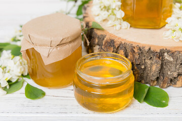 Sweet honey jar surrounded spring acacia blossoms. Honey flows from a spoon in a jar. jars of clear fresh acacia honey on wooden background