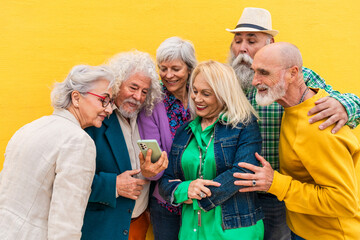 Cheerful elderly woman sharing smart phone with friends in front of wall