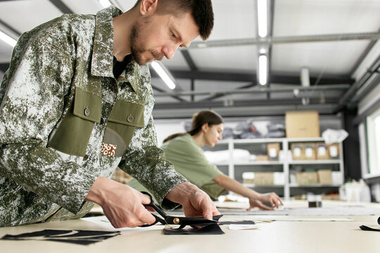 Focused fashion designer cutting sample with scissors at workshop