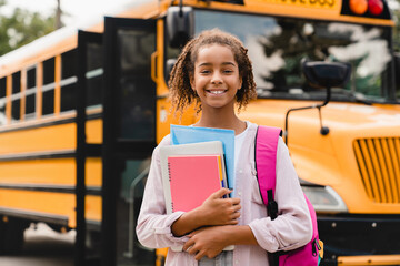 Smiling african-american schoolgirl going back to school with books and copybooks waiting for...