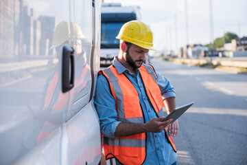 Logistics worker using tablet PC standing by truck