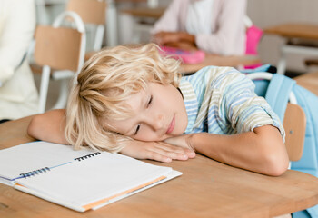 Sleepy tired bored schoolboy pupil student sleeping at the desk in school during the lesson class....
