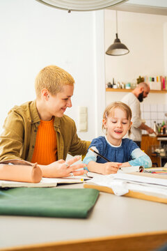 Smiling woman helping daughter studying at home