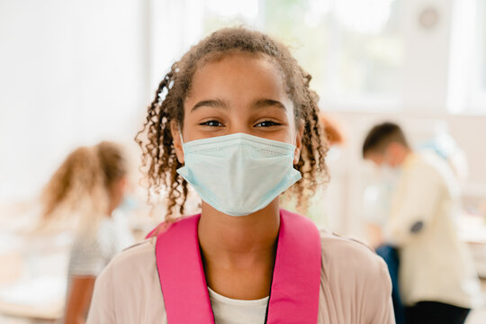 African-american schoolgirl kid pupil student wearing protective face mask against Covid19 coronavirus at lesson in school during pandemic.