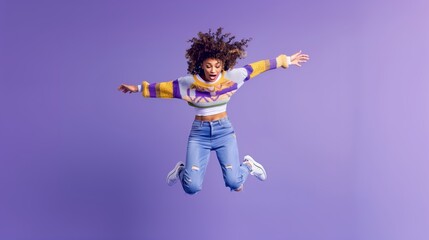 Obraz premium A girl is captured mid-jump in a studio, wearing a colorful sweater and jeans. The girl has a bright smile and exudes energy and happiness. The purple background adds a vibrant and playful