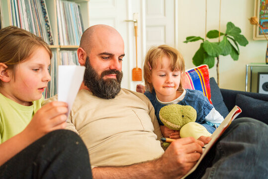 Father writing in book sitting with daughters on sofa at home