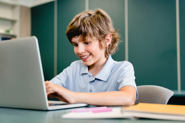 Smart caucasian kid schoolboy son pupil using laptop for doing homework projects e-learning distance education, online classes, lectures, playing computer games at school