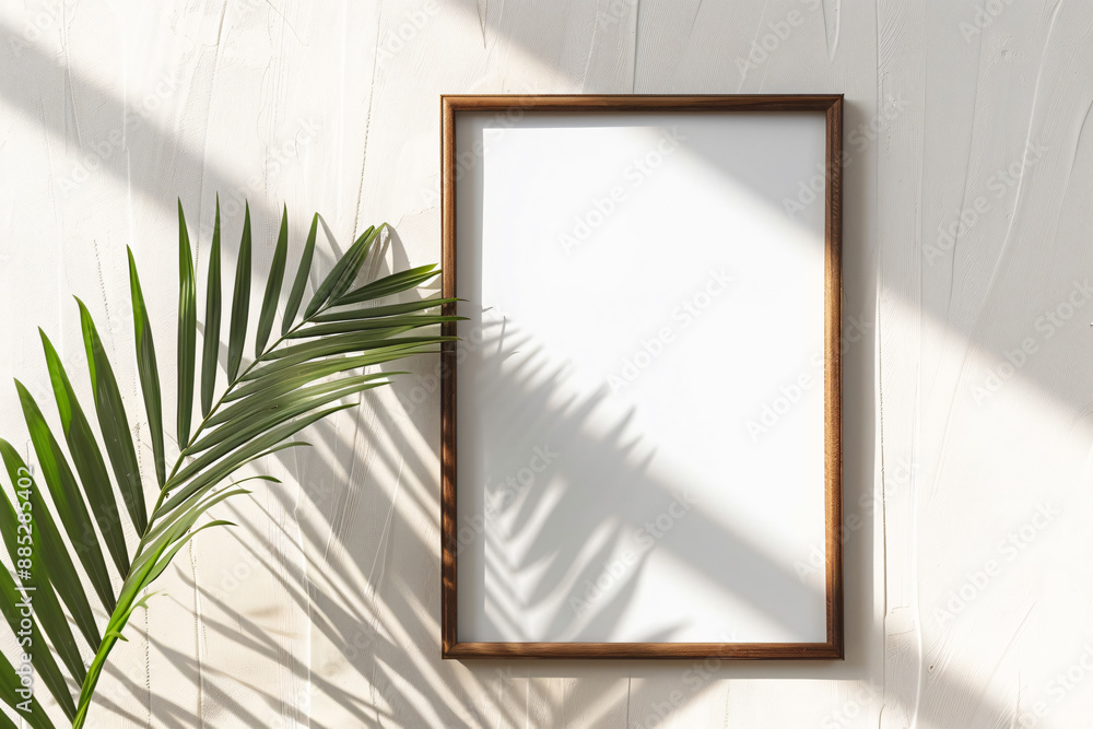 Poster photo of a vertical wooden frame mockup on white background with a palm leaf, creating an elegant an