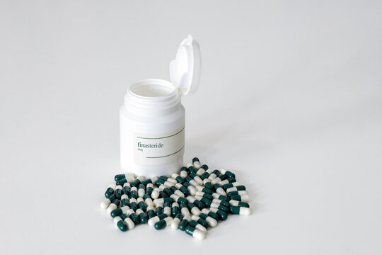 A pill bottle of 1mg finasteride capsules with several capsules scattered around