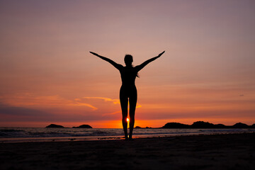 Silhouette of sport woman performing a yoga pose on the beach at sunset, with the sun setting behind the horizon and the calm sea .Yoga is meditation and healthy sport relaxing on summer holiday