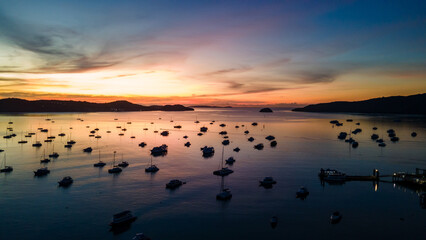 Aerial drone view of Chalong Pier in Phuket, Thailand. Sunrise silhouette scene. Many boats, yachts, sailboats and catamarans moored around the platform of Ao Chalong Bay.