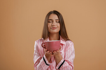 Drinking morning tea, holding cup. Young pretty woman is against background in the studio