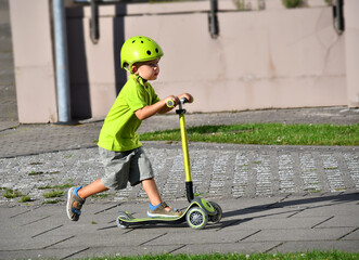 little toddler boy wearing safety helmet and riding kick scooter.