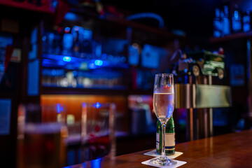 Bottle of Piccolo and a glass of chilled sparkling wine on a bar at night in a pub with colorful backlighting