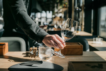 Close-up of waiter holding empty wine glass and placing it on the table