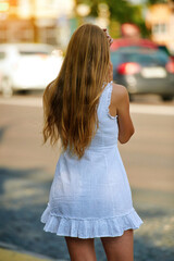  Woman in white summer dress stand alone at bus stop, view from back. Fashionable female in white dress waiting for bus. Brunette in trendy summer outfits.