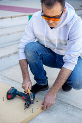 Man in protective eyewear using power drill outdoors vertical