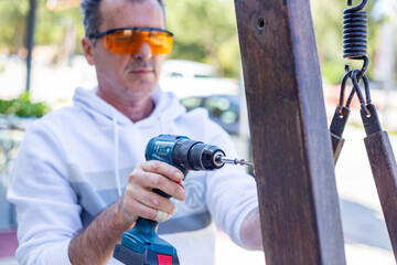 Naklejka premium Man in protective eyewear using power drill outdoors