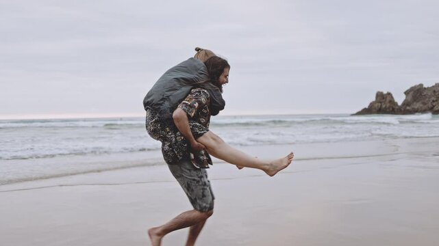 Joyful Gen Z couple enjoys fun summer evening at the beach, running, walking on sand in the ocean. Embracing love, happiness, smile, savor vacation together on the coast, creating lasting memories.