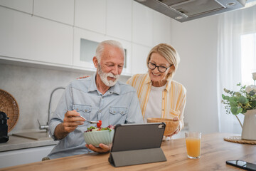Senior couple have breakfast together and use digital tablet