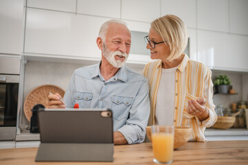 Senior couple have breakfast together and use digital tablet