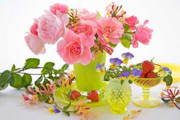 Pink roses and honeysuckle in a green vase against a white background still life