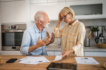 Serious angry senior couple calculate bills to pay domestic finances