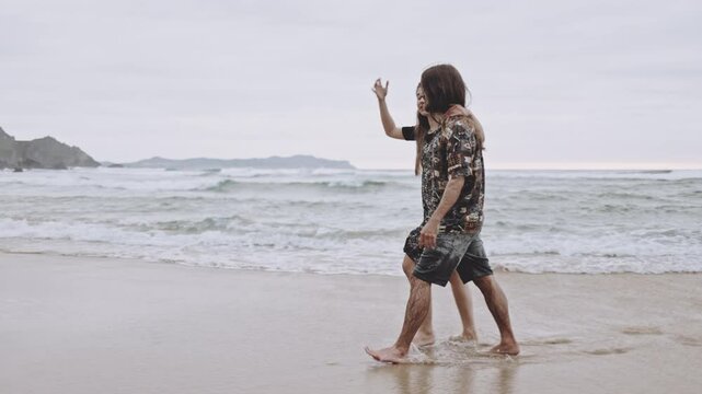 Joyful Gen Z couple enjoys fun summer evening at the beach, running, walking on sand in the ocean. Embracing love, happiness, smile, savor vacation together on the coast, creating lasting memories.
