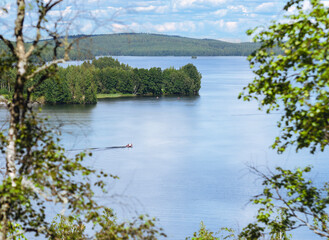 Aerial view of lake in Finland from a hill. A small boat traveling in the lake surface at summer time. Romantic vacation feelings near Himos and Jyväskylä Säynätsalo. Nice tourist spot