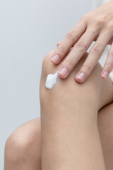 Cropped view of young woman applying body cream on her knees on gray studio background